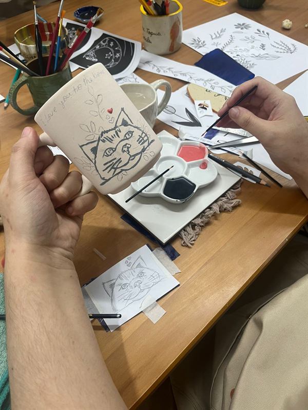 Aluno pintando um desenho de gato em uma caneca de cerâmica