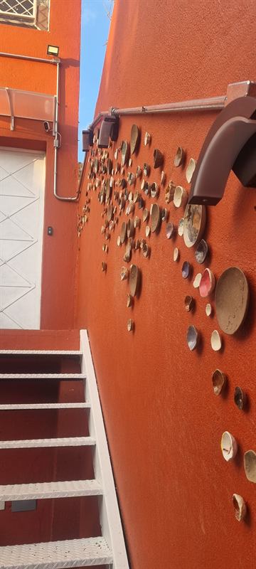 Parede laranja da escada do ateliê decorada com pratos e peças de cerâmica