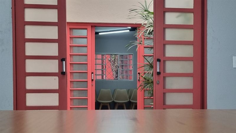 Portas vermelhas do ateliê com vista para uma sala com cadeiras verdes e planta pendurada