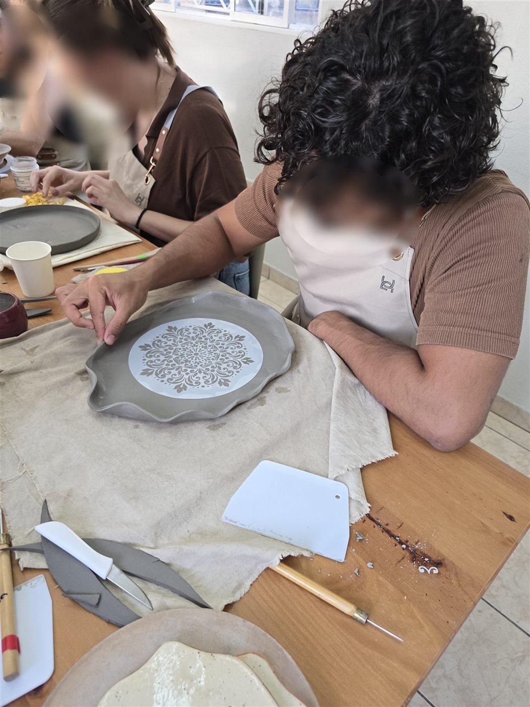 Participantes decorando pratos com estêncil de mandala, lado a lado