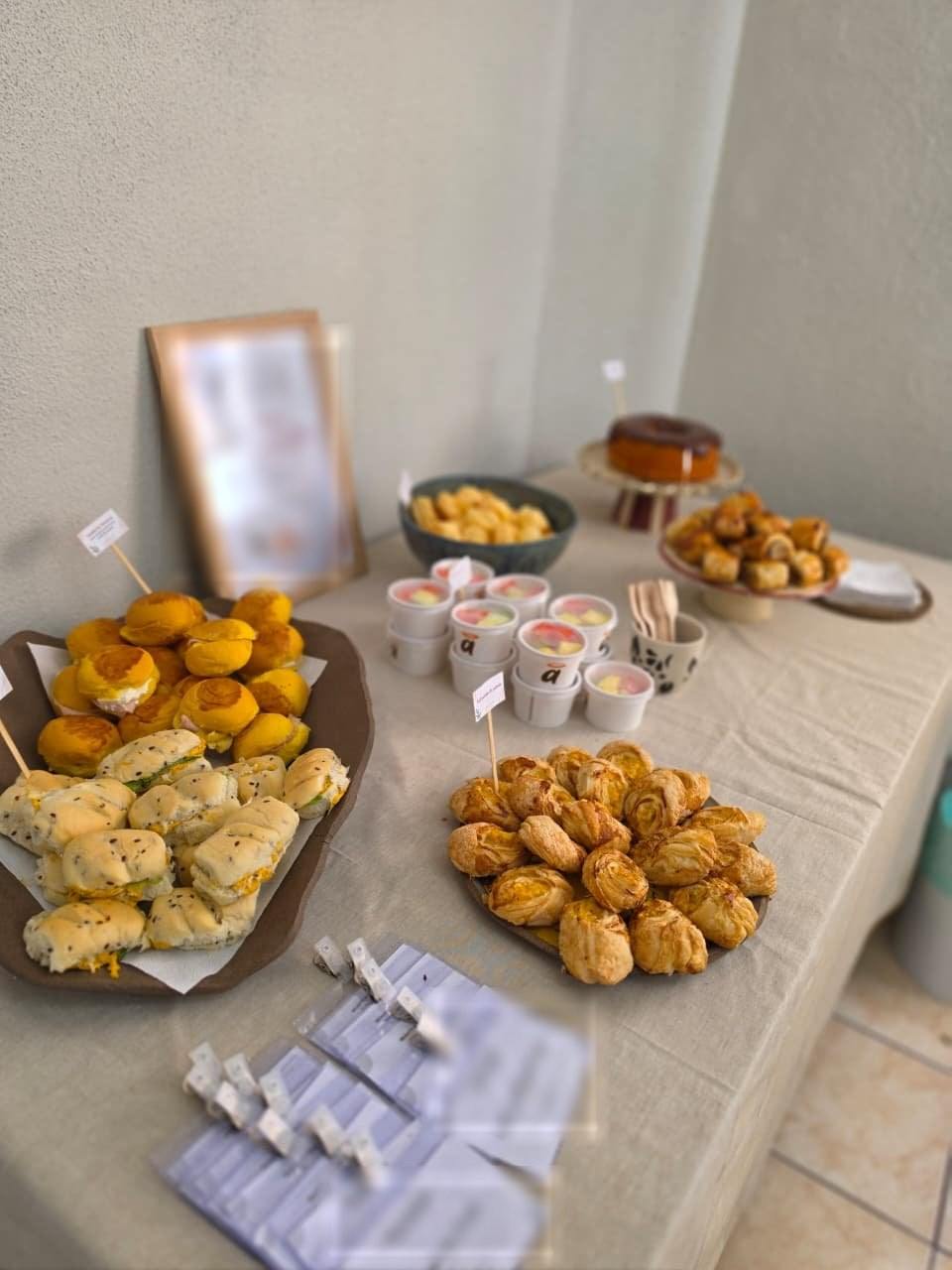Mesa de coffee break com sanduíches, folhados, bolo e copinhos de sobremesa