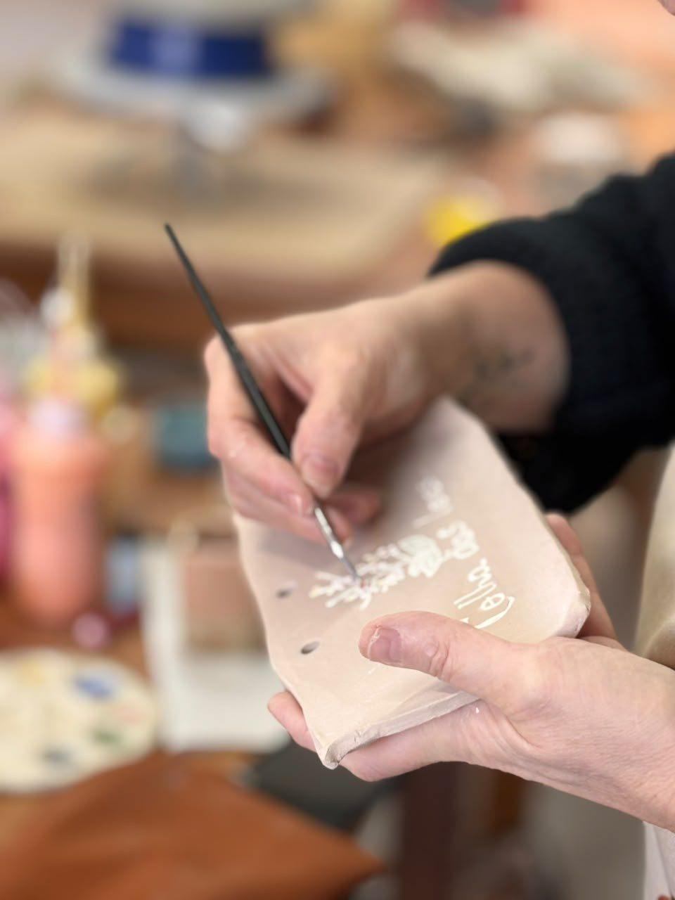 Mão pintando uma peça de cerâmica com pincel fino
