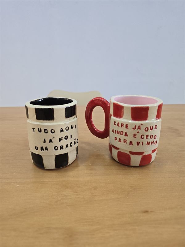 Duas xícaras de café de cerâmica, uma listrada em preto e branco e outra em vermelho e branco, com frases escritas